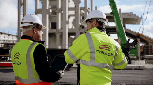 Two conack construction workers on site, holding a tablet, and discussing site safety at the building of a stadium