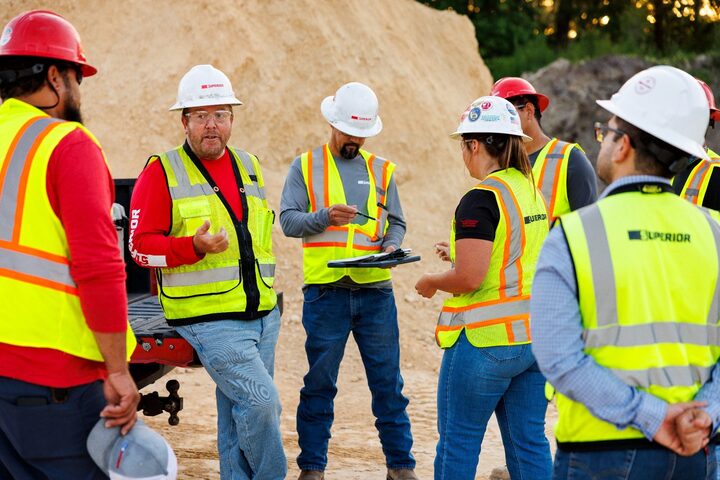 Superior Construction workers in hard hats and high-visibility vests discuss work at a civil construction site.