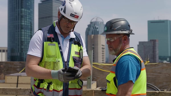 Shawn Dygd using HammerTech on his phone with a site worker at contractor Suffolk Construction’s Huntington Tower project in Boston.