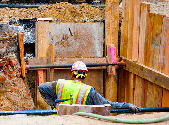 photo of a construction worker standing halfway inside a dug out hole, looking for risks before proceeding.