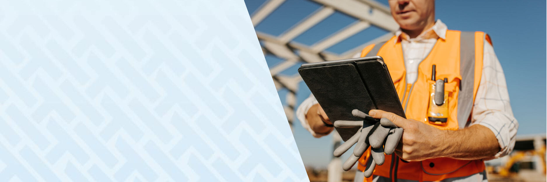 Shows a construction worker holding a tablet with PPE and walking through a construction site