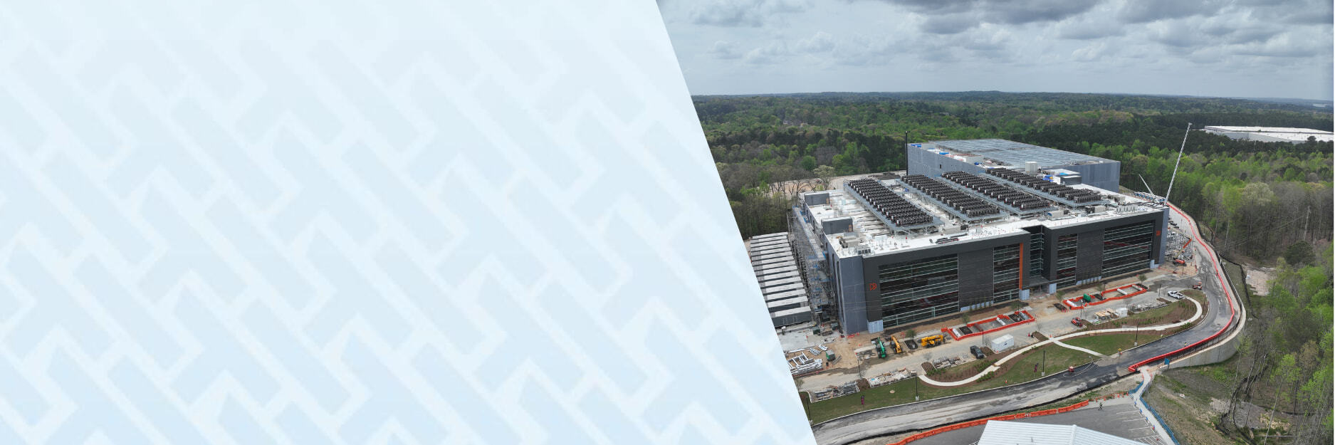 Drone view of a large-scale data center construction site by Brasfield & Gorrie using HammerTech for construction safety, featuring a multi-story building with extensive rooftop HVAC units, active construction zones, and a forested landscape in the background.