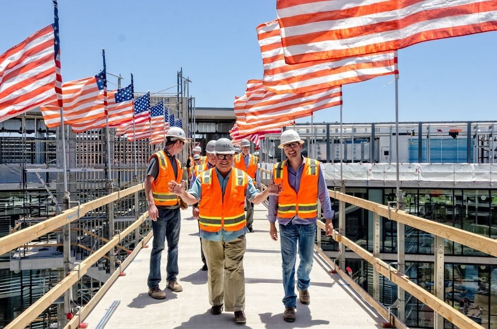 DPR Construction crew walking over a temporary bridge with US flags on each post and the wind blowing through the flags. 