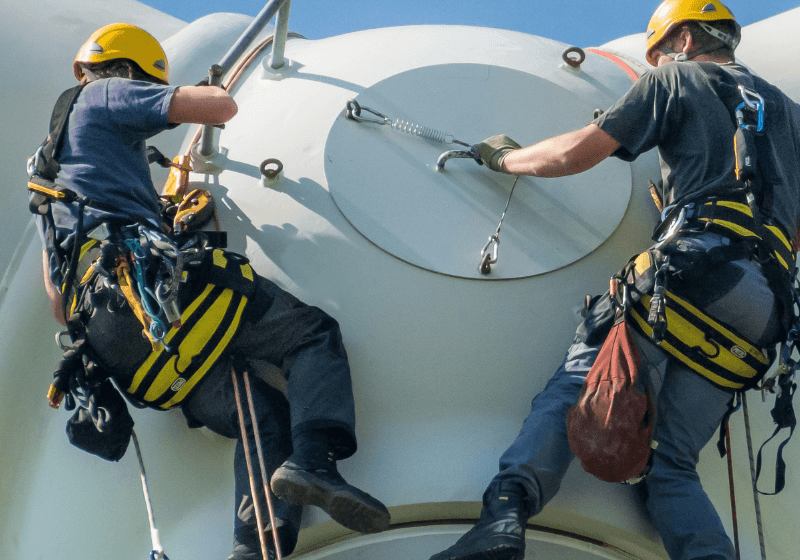 Image of two construction workers working and hanging from the top of a wind energy generator and using HammerTech Construction Safety Software platform for safety