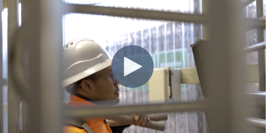 A construction worker signing in with facial recognition after passing through a construction site turnstile.
