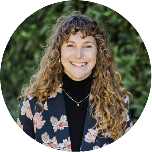 Georgia Bergers Headshot wearing floral blazer, white with curly long hair